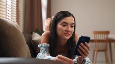 Kanepede yatan genç bir kadın internet bankacılığı için kredi kartıyla dizüstü bilgisayar kullanıyor. Evdeki online ödeme kapısından alışveriş yapıyor. Modern ve uygun online satın alma. Blithe
