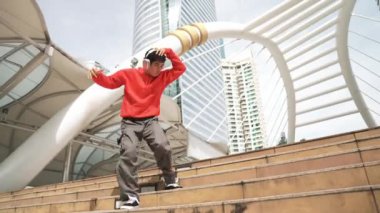 Şehre atlarken kulaklık takan Asyalı hippi. Profesyonel break dansçı şehirde break dans gösterisi yapıyor. Break dans ya da sokak dansı. Açık hava sporu 2024. Yumuşak bir şekilde..