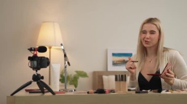 Sosyal medya için güzellik ve kozmetik video içeriği hazırlayan genç bir kadın. Güzellik blogcusu kamera ve ışık halkası kullanarak seyirciye ve takipçiye nasıl göz farı uygulanacağını gösteriyor. Blithe
