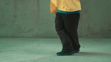 Profesyonel hipster sokak, şehir merkezinde ayak sesleri gösteriyor ya da pratik yapıyor. Genç break dansçı hareket ediyor ve kolunu ve bacağını esnetiyor. Açık hava sporu 2024. Gri arka plan. Hip hop modası. hiphop.
