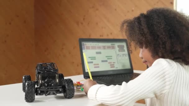 非洲女孩写作或汽车模型结构 而笔记本电脑显示代码 使用笔记本电脑的聪明学生开发程序或学习编程工程提示在Stem课上的应用 — 图库视频影像
