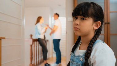 Stresli ve mutsuz genç kız arka planda ebeveynleri tartışırken köşede ağlayıp üzülüyor. Evde aile içi şiddet ve travmatik çocukluk depresyona dönüşür. Eşzamanlama