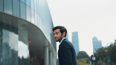 Profesyonel iş adamı hareket ediyor ve kameraya bakarken ayakta duruyor. Gülümseyen yönetici kameraya kendinden emin bir şekilde gülümsüyor. Mimari binada takım elbiseli yatırımcıların yakın çekimi. Sevinçli..