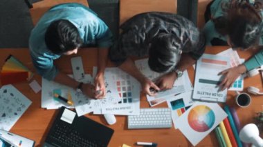 Tasarımcı fikirleri yazarken proje yöneticisinin yukarıdan aşağıya bakan görüntüsü. Akıllı iş adamları logo tasarımı fikrini açıklarken tasarımcılar palete bakarken temayı seçiyorlar. Sempozyum.