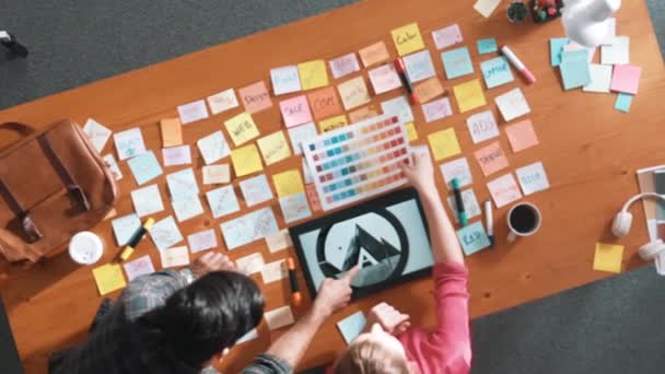 カラーパレットから色を選択するために一緒に働くビジネスの人々のトップビュー プロジェクトマネージャーは ロゴグラフィックを見ているビジネスマンしながら マーケティングチームにタブレットを使用してアイデアを提示します シンポジウム — ストック動画