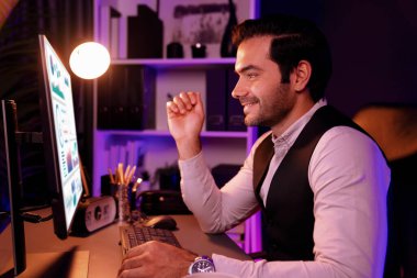 Gülümseyen zeki işadamı, uzaktan da olsa satış ekibiyle çevrimiçi olarak buluşuyor ve gece vakti Neon Dark Light Home Office 'deki bilgisayar ekranında ürün veritabanındaki araştırma hedef pazarını tartışıyor. Tahmin et..