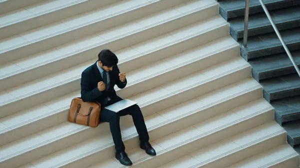Top view business man celebrate successful project while sitting at stairs. Smart project manager getting new gob, getting promotion, increasing sales while calling friends by using laptop. Exultant.
