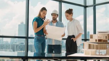 Proje planına bakarken tasarımla ilgili düşünen, paylaşan, beyin fırtınası yapan profesyonel mimar mühendis takımı. Genç bir mimar, genç ve güzel bir menajer not alırken elinde bir plan tutuyor. İzleme