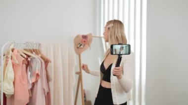 Genç sosyal medyum kadın selfie çubuğuyla moda videosu yapıyor. Blogcu kameraya gülümserken çevrimiçi kıyafetleri izleyicilere ya da takipçilere vlog sattırıyor. Blithe