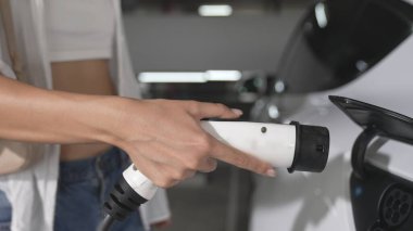 Genç hareketli kadın, EV elektrikli arabasıyla şehir merkezindeki alışveriş merkezinin otoparkına gidiyor. Sürdürülebilirlik yaşam tarzını yeşil, temiz, yeniden şarj edilebilir elektrikli araç iç organlarıyla şarj ediyor.
