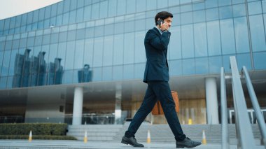 Akıllı iş adamı binada yürürken telefonla konuşuyor. İş planı, pazarlama stratejisi ya da çalışma hakkında konuşmak için akıllı telefonla konuşurken sokakta yürüyen mutlu bir yönetici. Sevinçli..