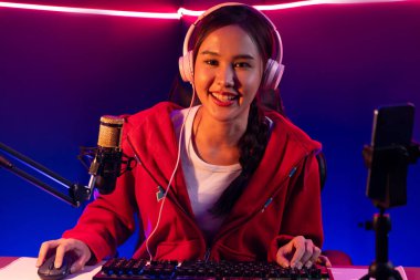 İnternet üzerinden kulaklık takıp gülümseyen Asyalı güzel kız flamasının sunucu kanalı izleyicilerle internet üzerinden konuşma yapıyor. Esport yetenekli takım oyuncuları neon mavi odada. Taktik.