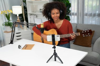 Genç Afrikalı Amerikalı müzisyenin sunucu kanalı gitar çalıyor, şarkı söylüyor, stüdyoda akıllı telefondan yayın yapıyor. Ekipman kulaklıkları dekorasyonu ve mikrofon kaydı. Tatlandırıcı.