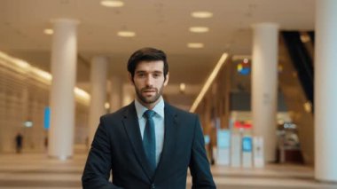 Modern bir alışveriş merkezinde kolları bağlı duran bir iş adamı ortada yürüyor. Gülümseyen mutlu yatırımcı, arka planı bulanık bir şekilde kollarını kavuştururken kameraya özgüvenle bakıyor. Sevinçli..