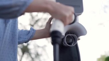 Kapalı alan kadını, doğal yeşil parktaki otoparkta EV elektrikli araba aküsünü şarj ediyor. Sürdürülebilir ve çevre dostu seyahat için şarj edilebilir araç için temiz enerji teknolojisi. Titiz