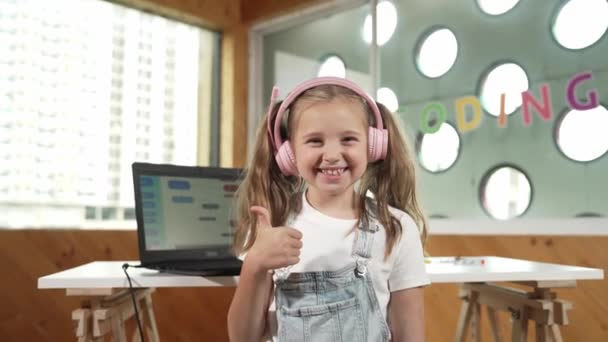 一个漂亮的高加索女孩在镜头前微笑着 同时伸出一个大拇指向上的手势 小孩戴着耳机 穿着休闲装 站在那里看着相机 Erudition — 图库视频影像