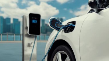 Elektrikli araba şarj istasyonuna bağlanır ve şehrin arka planında gelişmiş EV şarj cihazıyla şarj edilir. Gelecekteki yenilikçi çevre dostu enerji sürdürülebilirliği CO2 emisyonunu azaltmak için. İnceleyin