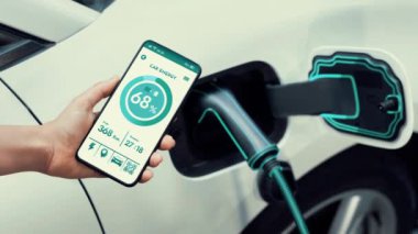 Akıllı telefon akü durumu arayüzünü elinde tutan iş kadını akıllı EV mobil uygulama ile otomobil parkındaki şarj istasyonundan elektrik şarj eden çevre dostu EV araba. İnceleyin