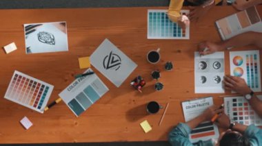 Proje yöneticisi renk paletleri seçerken tasarımcının tablete baktığı yukarıdan aşağıya hava görüntüsü. Profesyonel grafik tasarımının en üst görüntüsü ve logoya bakın. Yetenekli ekip grafikleri seçiyor. Sempozyum.