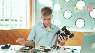 Liseli çocuk, dizüstü bilgisayarlı ve elektrikli aletli araba modelini tamir ediyor. BTMM sınıfında eletronik ekipman kullanırken, gençlerin robot makine inşaatını denetlemesi. Öğretim