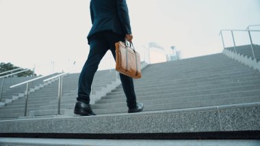 Akıllı bir iş adamının elinde çantayla merdivenlerden yukarı çıkışının en üst görüntüsü. Profesyonel proje yöneticisi merdivenlerden çıkıp işyerine gidiyor. Yeteneklerini arttırmak, terfi almak, seyahat etmek. Sevinçli..