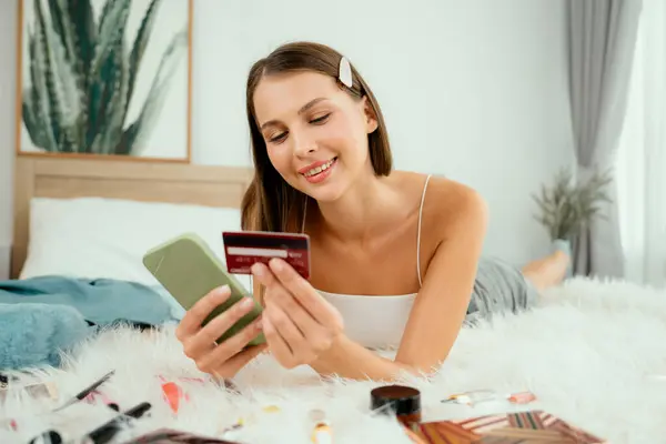 年轻女子躺在床上 用在线支付应用程序和智能手机上的数字钱包支付信用卡 电子商务购物和通过移动互联网进行现代采购 — 图库照片