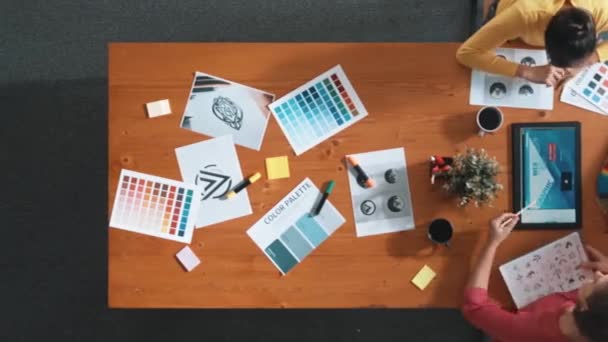 カラーパレットを選ぶプロジェクトマネージャーの間 タブレットを見ているデザイナーの空中ビューをトップダウン 熟練したグラフィックデザインのタイムラウンドとロゴを見てください グラフィックを選択する熟練チーム シンポジウム — ストック動画