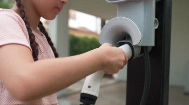 Küçük mutlu kız, EV şarj istasyonundan elektrikli aracı şarj ederken çevre dostu ve enerji sürdürülebilirliğini öğreniyor. EV araba ve sürdürülebilir gelecek nesil konsepti. Titiz