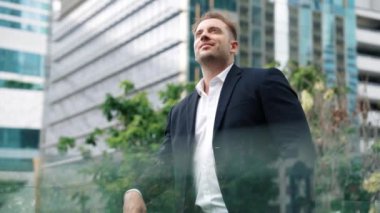 Kafkasyalı iş adamı cep telefonunu tutuyor ve gökdelen manzarasına bakıyor. Modern binanın çatısında duran yetenekli erkek lider. Kafkasyalı yönetici gözlerini dinlendirirken telefona bakar. Urbane.