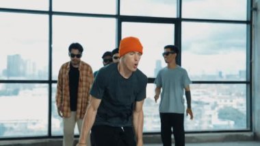 Profesyonel hipster, çeşitli çok kültürlü arkadaşlarıyla birlikte adım atıp dans ediyor. Gökyüzü dövüşçüsü ve şehir manzaralı pencerenin yanında duruyor. Break dans. Açık hava sporları konsepti 2024 hiphop..
