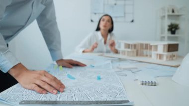 Ev modeliyle çalışan yetenekli beyaz tasarımcı Asyalı mimar mühendis ile toplantı masasında üzerinde taslak ve ev modeli dağınıklığı olan ev planlarını tartışırken. Tertemiz..
