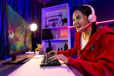 Host channel of young beautiful Asian gaming streamer playing fighting Moba at battle arena game on pc screen with multiplays, wearing pastel headphone at neon digital light modern room. Stratagem. clipart