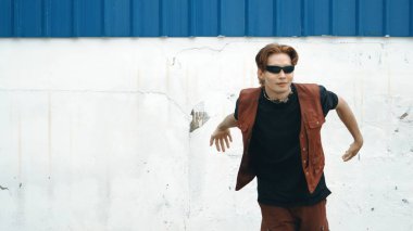 Beyaz arka planda break dans pratiği yapan yakışıklı bir sokak dansçısı. Hip hop tarzı giyinen sporcu, mavi arka planlı bir sokakta müzik eşliğinde ayak sesleri çıkarıyor. Açık hava sporu 2024. ÇalışmaComment.