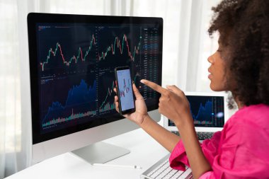 Ciddi yüzlü Afrikalı kadın blogcu, ekran ekranına bakıyor ve borsa başarısı yüksek olan akıllı telefona bakıyor. Çevrimiçi bilgisayar ticaretinde döviz yatırımı kavramı. Tatlandırıcı.