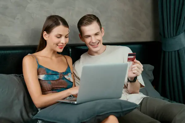 stock image Young couple sit in the home bedroom using online payment app and digital wallet on smartphone to pay with credit card. E commerce shopping and modern purchasing via mobile internet. Unveiling