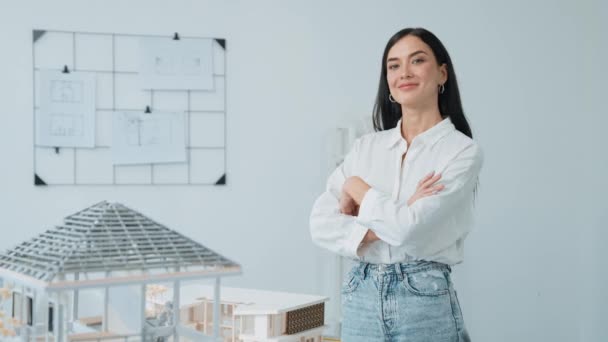 年轻美丽的专业建筑工程师的密切的肖像交叉双臂 自信地与房子模型在白色的现代办公室与蓝图 创意生活和设计 纯洁无瑕 — 图库视频影像
