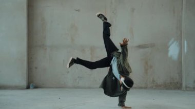 Hippi, şehir caddesinde hip-hop dinlerken kulaklık takıyor. Sokak dansçısı ayak seslerini kulaklıktan müziğe taşıyor. Açık hava sporu 2024. Çimento arka planı. Moda. Aktif stil. hiphop.