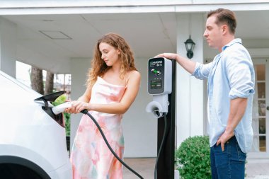 Çevre dostu, mutlu ve sevimli çift EV şarj istasyonundan elektrikli aracını şarj ediyor. EV araba teknolojisi gelecekteki sürdürülebilirlik için kullanılıyor. Eşzamanlama