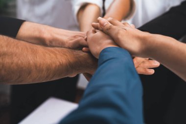 Çeşitli ofis çalışanlarından oluşan bir grup, ofis odasında el ele vererek iş sinerjisini ve iş yerindeki güçlü verimli takım çalışmasını sembolize ediyor. İş çalışanları arasındaki işbirliği ve birlik. Tedbirli