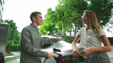 Yavaş çekim çift yazın yeşil sürdürülebilir şehir açık bahçesinde elektrikli araba şarj ile seyahat elektrikli aracın temiz yeniden şarj edilebilir enerjisi için kentsel sürdürülebilirlik yaşam tarzı olarak