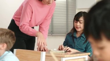 Öğretmen sınıfları kontrol ederken Asyalı kız yazı yazıyor ya da not alıyor. Kafkasyalı öğretmen çeşitli öğrenciler fen dersinde çalışırken mutlu öğrencilerin sınav ya da sınıf çalışmalarına yardım eder. Eğitim. Pedagoji.