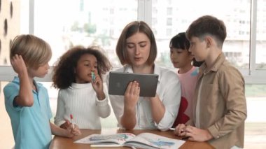 Bir grup öğrenciye çevrimiçi ders verirken elinde tablet tutan akıllı öğretmen. Yetenekli eğitmen mühendislik derslerini anlatırken genç öğrenci oturuyor ve sunumu dinliyor. Etkinlik.