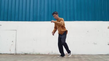İspanyol adam kollarını açıp duvarın önünde dans ediyor. Dansçı ya da koreografın günlük kıyafetleriyle hip hop tarzında break dans yaparken ki görüntüsü. Açık hava sporu 2024 hiphop..
