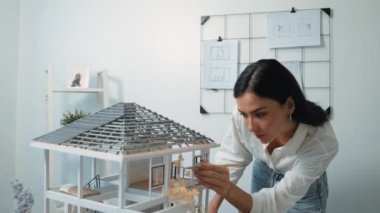 Genç, güzel ve zeki mühendisin yakın çekimleri modern ofiste duvarında taslak olan kalem kullanarak ev modelini ölçmeye odaklanıyor. Yaratıcı yaşam ve tasarım konsepti. Tertemiz..
