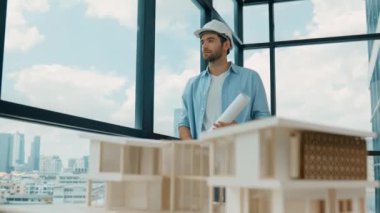 Gökdelen manzarasına bakarken yürüyen profesyonel mimar mühendisi. Masaya yerleştirilmiş ev modeliyle pencereye bakarken yetenekli proje yöneticisi proje planını tutuyor. Tasarım. İzleme