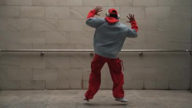 Yakışıklı koreograf gri arka planda sokak dansı yapıyor. Genç çekici erkek dansçı şık kıyafetler giyerken gösteri yapıyor. Hareketli bir adım. Uzayı kopyala Açık hava sporu 2024. Yumuşak bir şekilde..