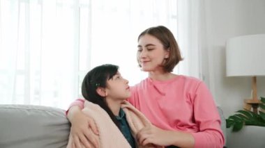 Kafkasyalı anne kızını kucaklıyor ve kanepede oturuyor ve alnından öpüyor. Mutlu anne oturma odasında sevimli Asyalı liseli kıza sevgi ve sevgi gösteriyor. Güzel bir aile birlikte vakit geçirir. Pedagoji.