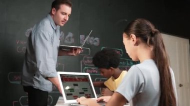 Afrikalı erkek manken tamir ederken beyaz kız programlama ya da kodlama sistemi. Öğretmen elinde dizüstü bilgisayar tutarken çeşitli çocukların web geliştirme programı yazmalarına bakıyor. Yenilik eğitimi. Öğretim