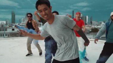 Bir grup çok kültürlü hippi çatıda işaret fişeği çalıyor. Zenci dumanı tutan çekici bir sokak dansçısı hip-hop müzik eşliğinde break dans yapıyor. Açık hava sporu 2024. Sokak dansı. hiphop.