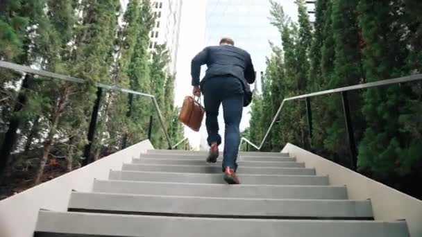 高加索商人走上楼梯 用智能手机给经理打电话 回顾经理在上楼时通过电话与营销团队交谈和计划财务策略的情景 城市E — 图库视频影像